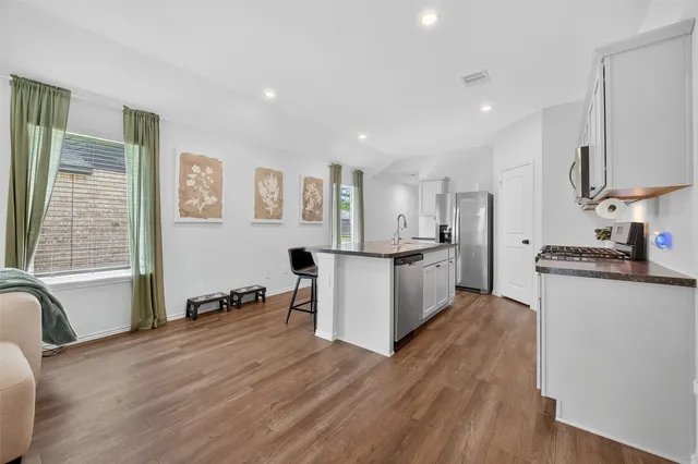 a large white kitchen with stainless steel appliances granite countertop a stove a sink a refrigerator white cabinets and wooden floor next to a window