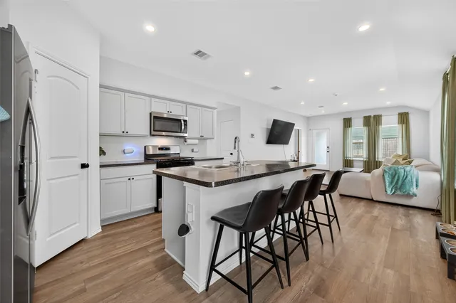 a kitchen with stainless steel appliances granite countertop a stove a refrigerator a sink a dining table and chairs with wooden floor