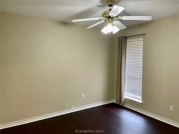 an empty room with wooden floor chandelier fan and windows