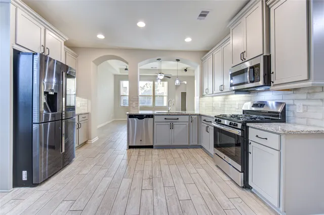 a large kitchen with stainless steel appliances granite countertop a large stove top oven a refrigerator cabinets and wooden floor