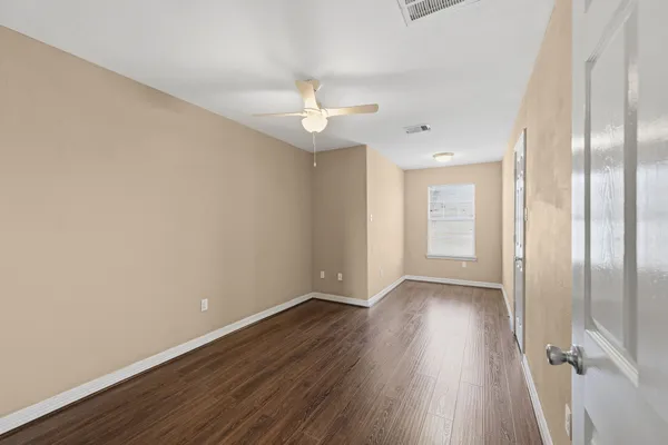 an empty room with wooden floor fan and windows