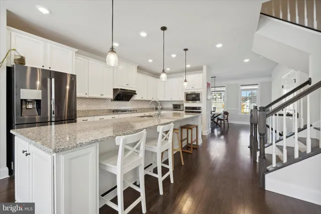 a kitchen with stainless steel appliances kitchen island granite countertop a stove a refrigerator a oven a dining table and chairs with wooden floor