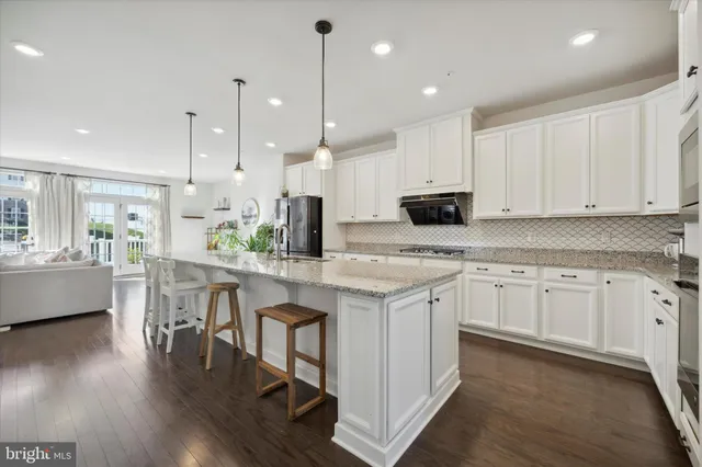 a kitchen with stainless steel appliances granite countertop a sink a stove a refrigerator and white cabinets with wooden floor