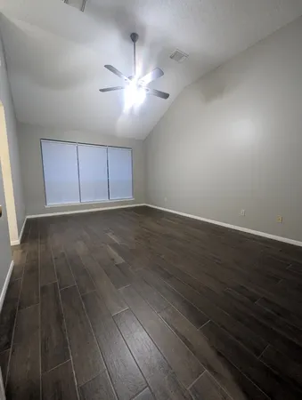 a view of an empty room with wooden floor and a ceiling fan