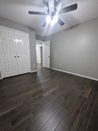 an empty room with wooden floor chandelier fan and windows