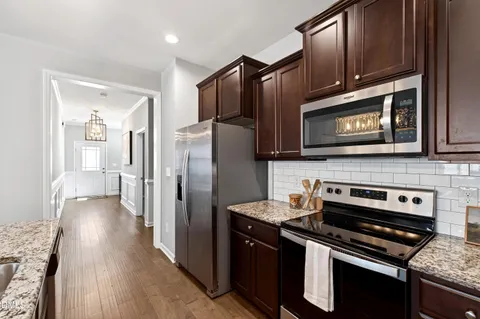 a kitchen with granite countertop a refrigerator a stove a sink and a dining table with wooden floor