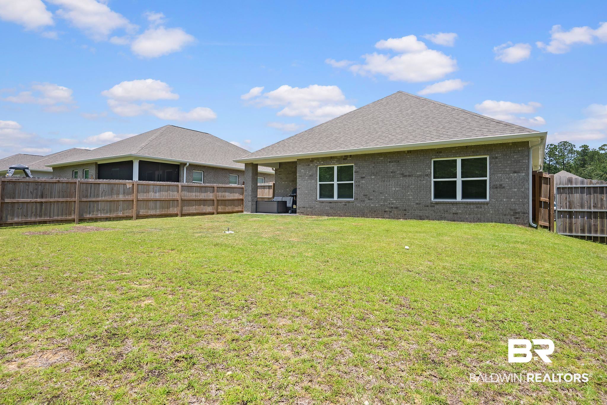 13966 Antler Hl Road Daphne, AL 36527 - Photo 34 of 44 Expansive grassy yard featuring a private wood fence, a grey brick exterior, a grey shingle roof, and multiple windows