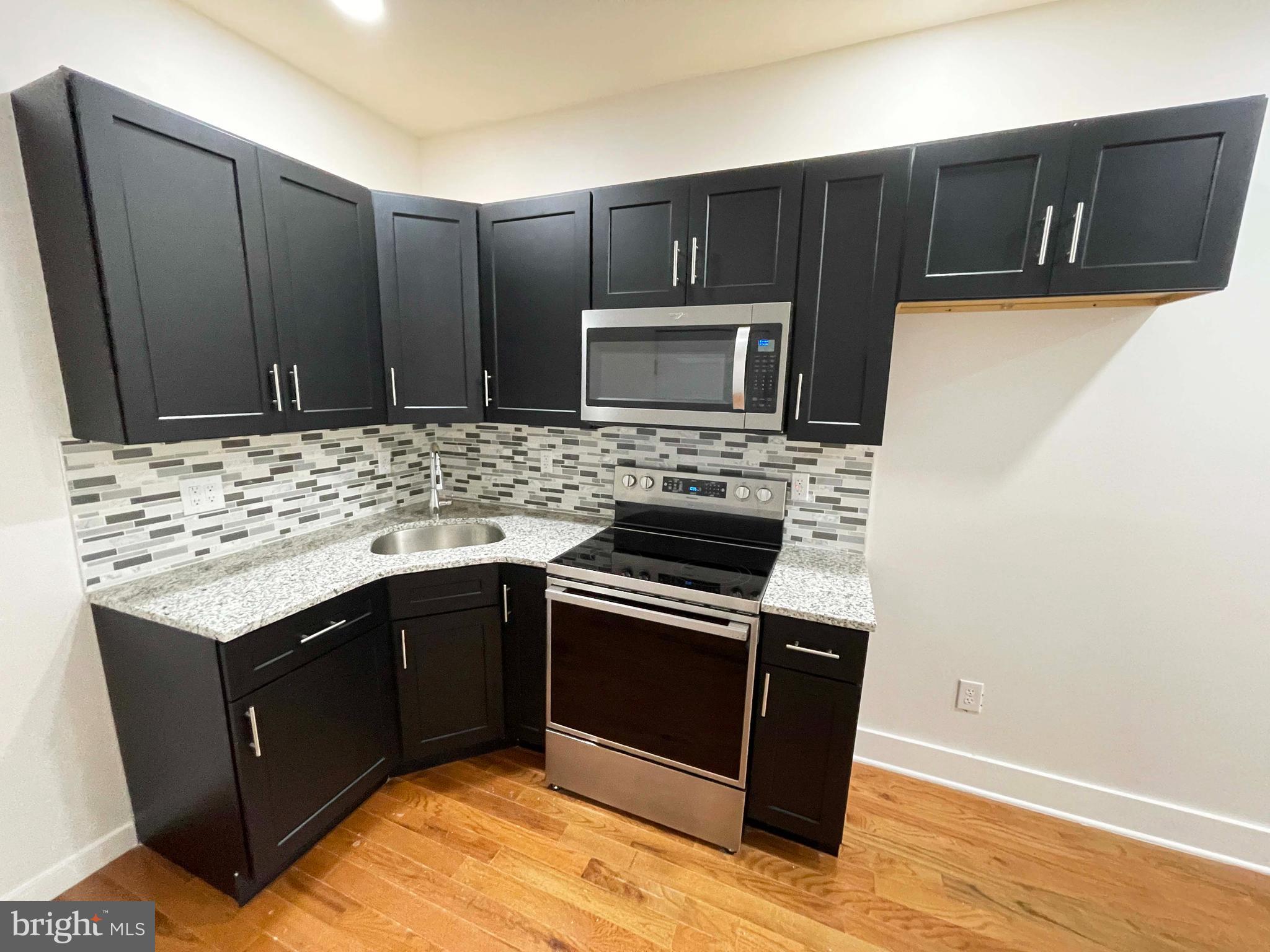 309 South 60th Street, Unit 1 Philadelphia, PA 19143 - Photo 11 of 17 a kitchen with stainless steel appliances wooden cabinets and granite counter tops