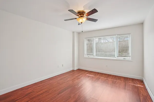 a view of an empty room with wooden floor and a ceiling fan