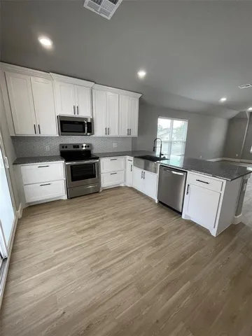 a large kitchen with granite countertop a stove top oven a sink dishwasher and a refrigerator with wooden floor