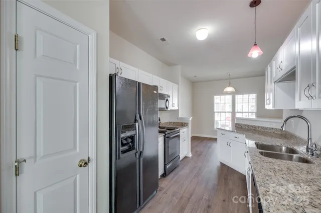 a kitchen with stainless steel appliances granite countertop a refrigerator a sink dishwasher a stove and white countertops with wooden floor