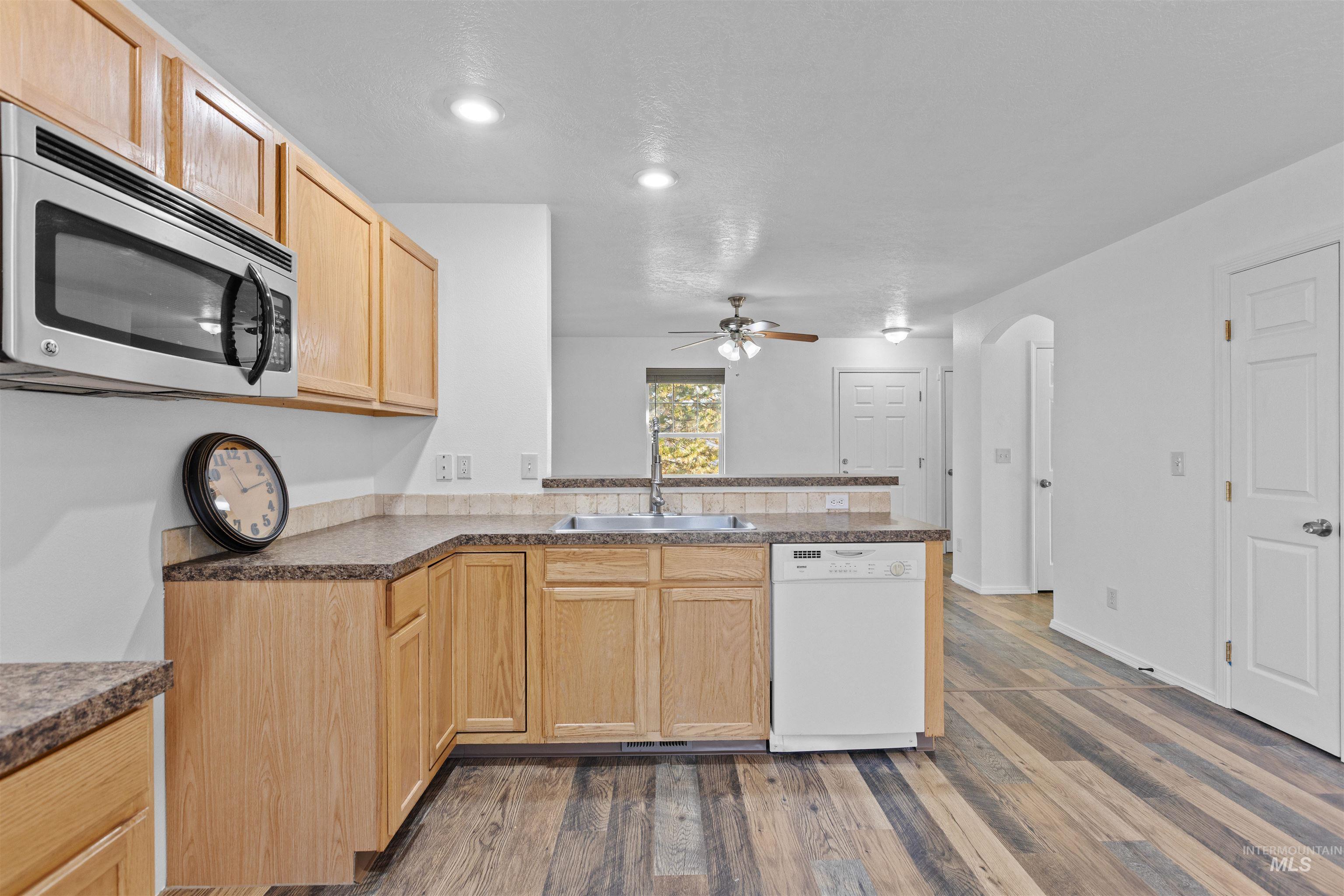 16535 Chino Avenue Caldwell, ID 83607 - Photo 13 of 26 Kitchen featuring a peninsula, arched walkways, stainless steel microwave, white dishwasher, and light brown cabinetry