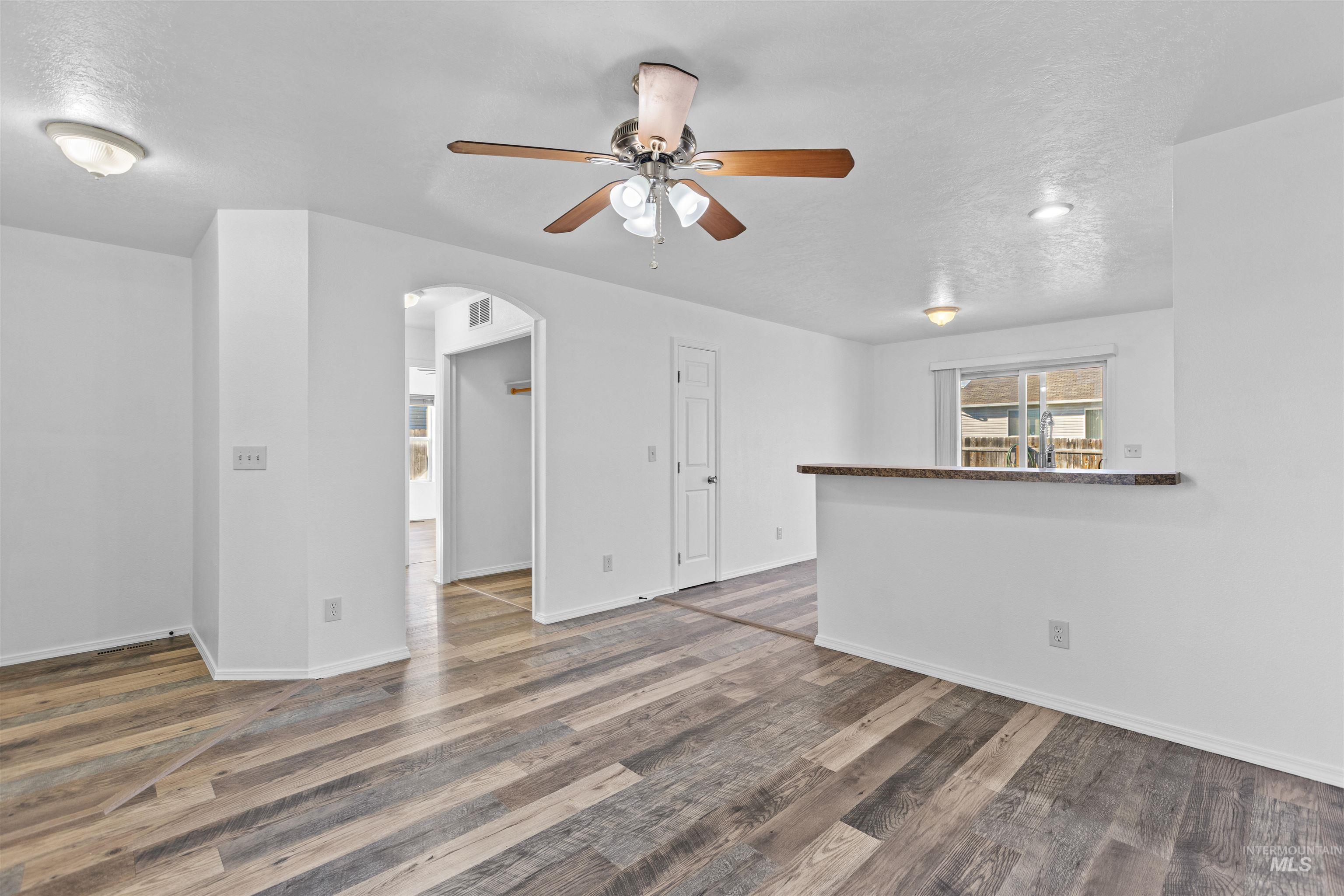 16535 Chino Avenue Caldwell, ID 83607 - Photo 6 of 26 Unfurnished room with a textured ceiling, a ceiling fan, arched walkways, and dark wood-style floors