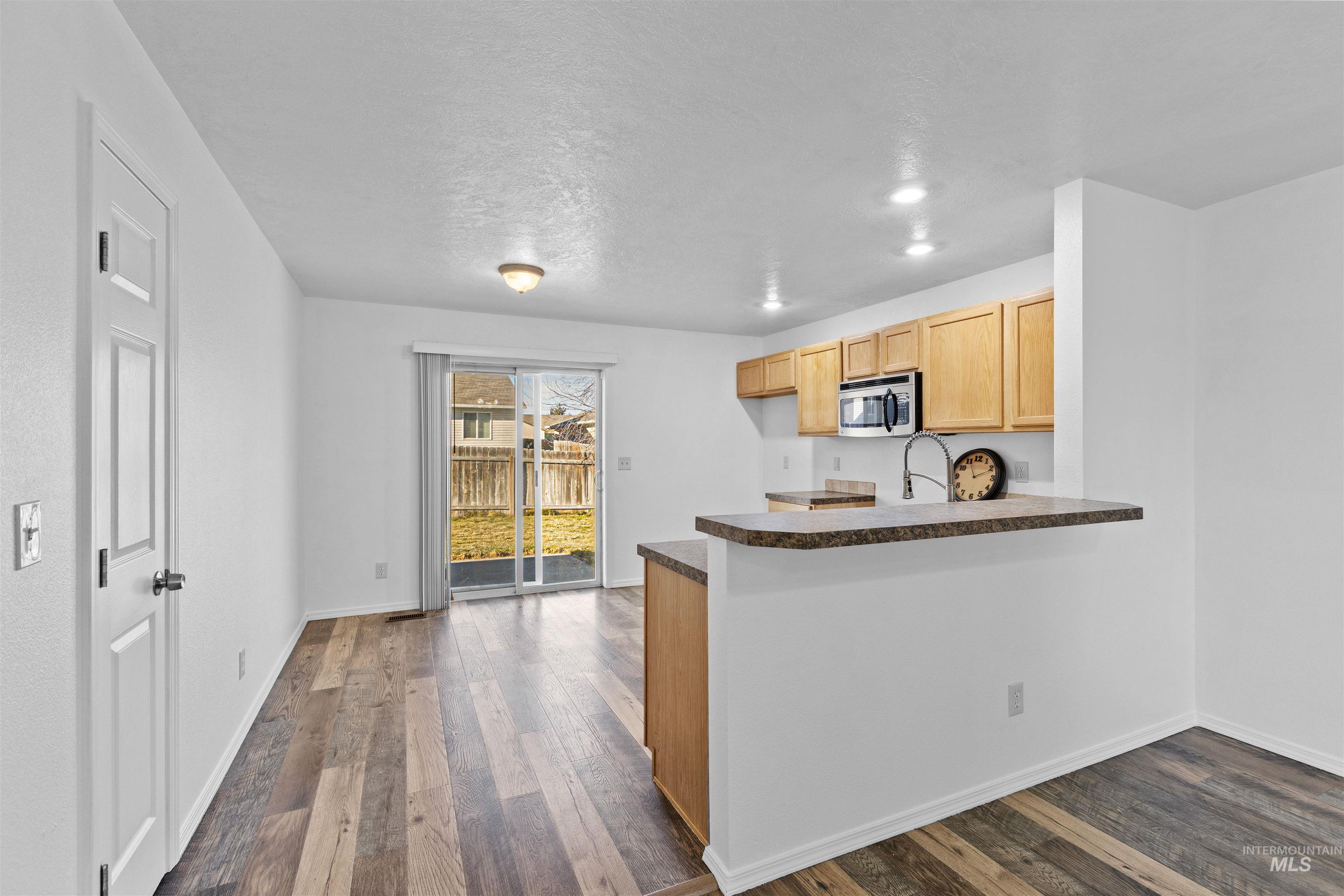 16535 Chino Avenue Caldwell, ID 83607 - Photo 9 of 26 Kitchen featuring dark wood-style floors, light brown cabinetry, dark countertops, stainless steel microwave, and a peninsula