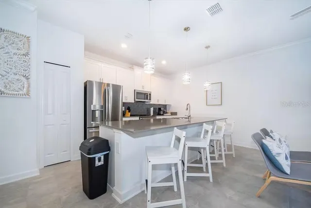 a kitchen with stainless steel appliances kitchen island granite countertop a dining table chairs and a refrigerator