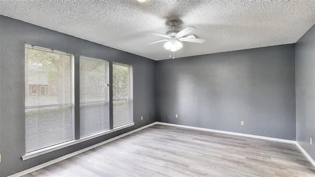 an empty room with wooden floor fan and windows