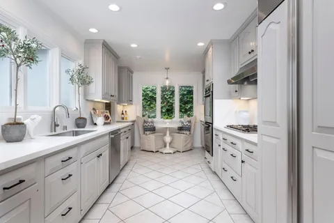 a large white kitchen with stainless steel appliances granite countertop a large stove a sink dishwasher and white cabinets with wooden floor