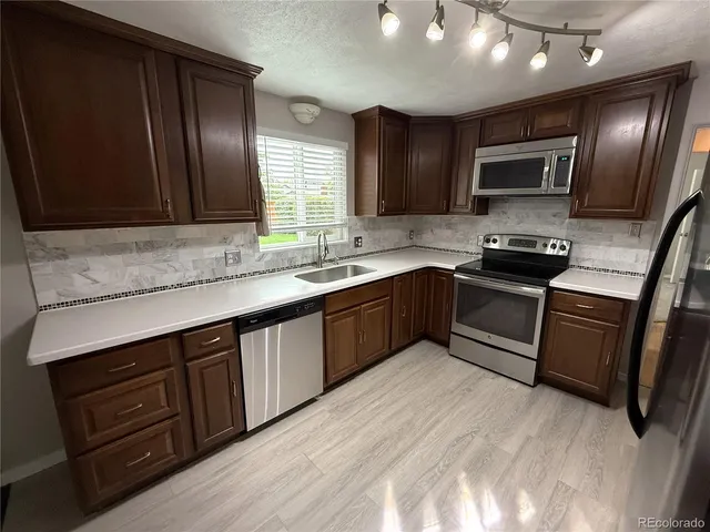 a kitchen with stainless steel appliances granite countertop wooden cabinets a sink dishwasher a stove and a refrigerator with wooden floor