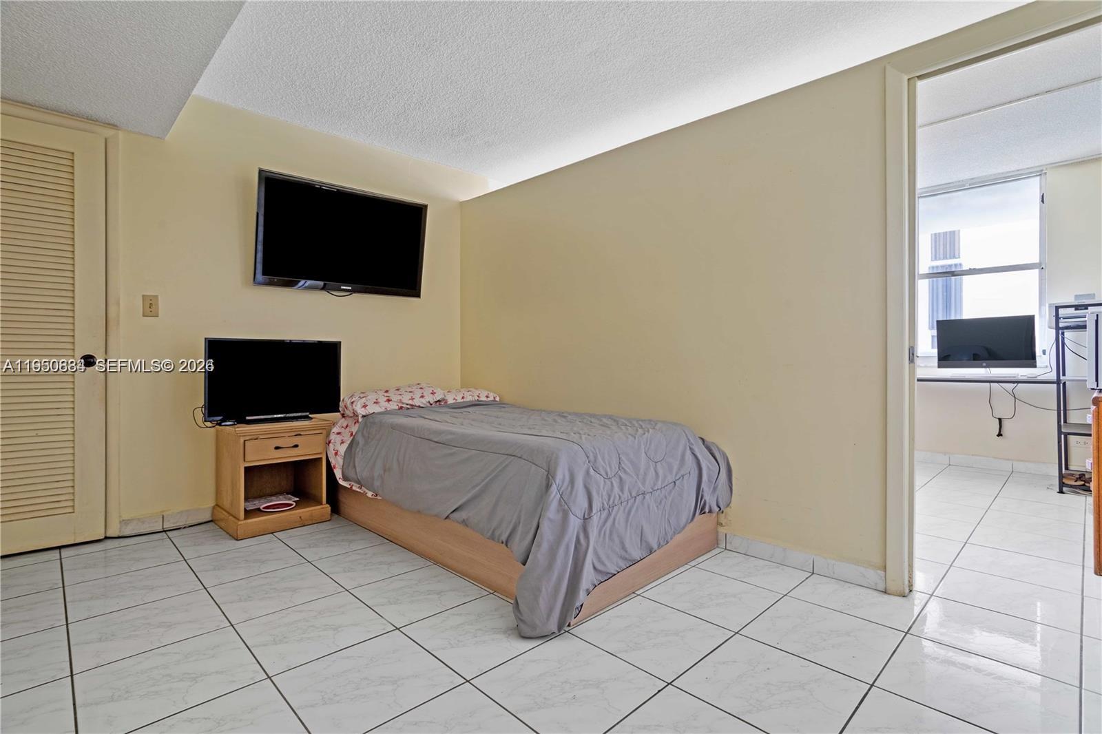 6039 Collins Avenue, Unit 809 Miami Beach, FL 33140 - Photo 13 of 14 a spacious bedroom with a bed and a flat screen tv