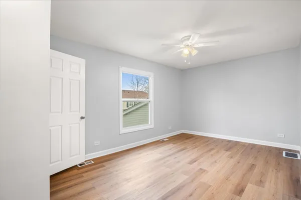 an empty room with wooden floor chandelier fan and windows