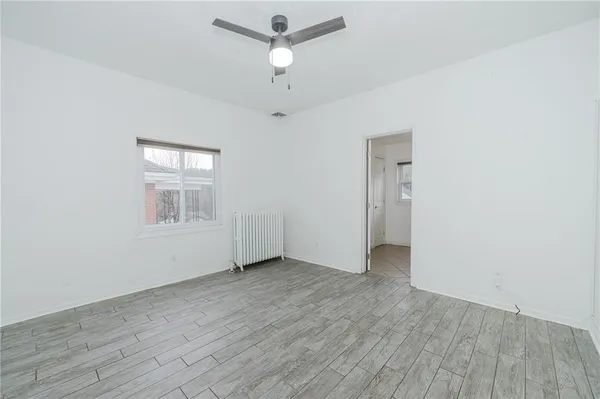 an empty room with wooden floor ceiling fan and windows