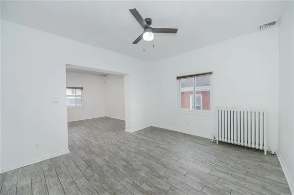 an empty room with wooden floor a ceiling fan and windows