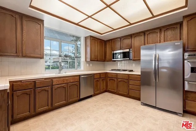 a kitchen with stainless steel appliances granite countertop a refrigerator a sink a stove a microwave and wooden cabinets