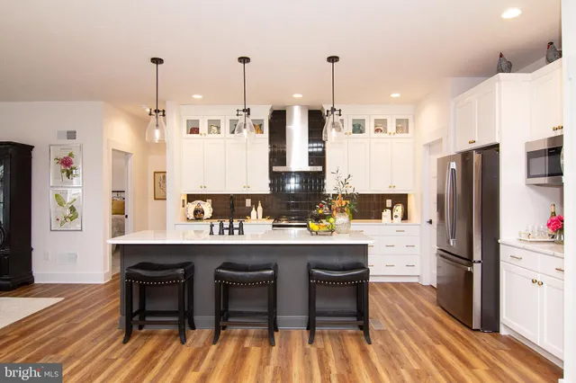 a kitchen with stainless steel appliances kitchen island granite countertop a sink a stove a refrigerator and white cabinets with wooden floor