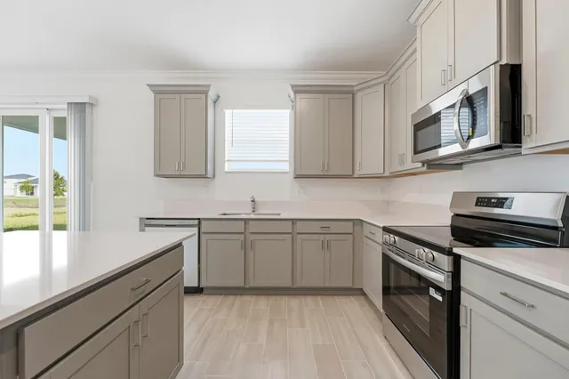 a kitchen with stainless steel appliances granite countertop white cabinets a sink a stove a microwave and wooden floors