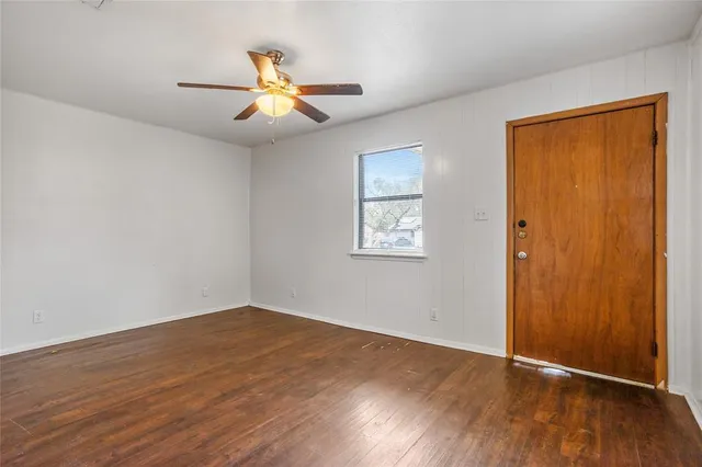 a view of an empty room with wooden floor and a ceiling fan
