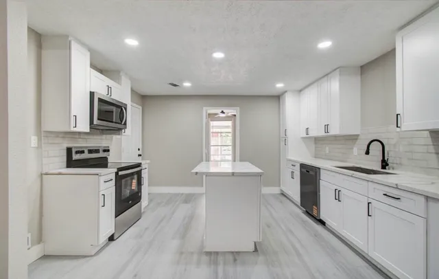 a large kitchen with stainless steel appliances granite countertop a stove top oven a sink dishwasher and white cabinets with wooden floor