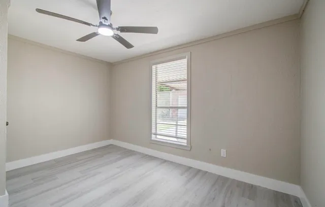 an empty room with wooden floor ceiling fan and windows