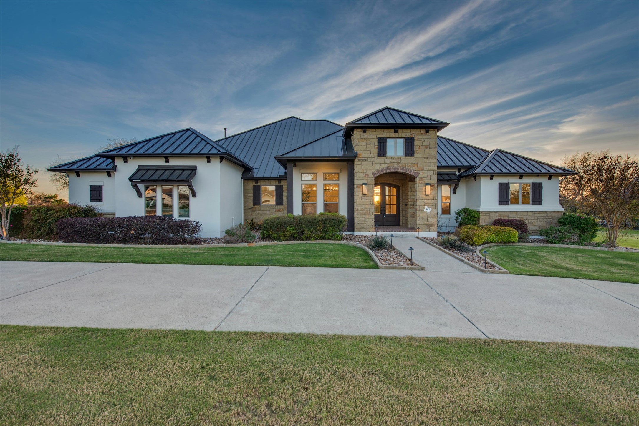 View of front of house with a standing seam roof, a front lawn, stone siding, and stucco siding