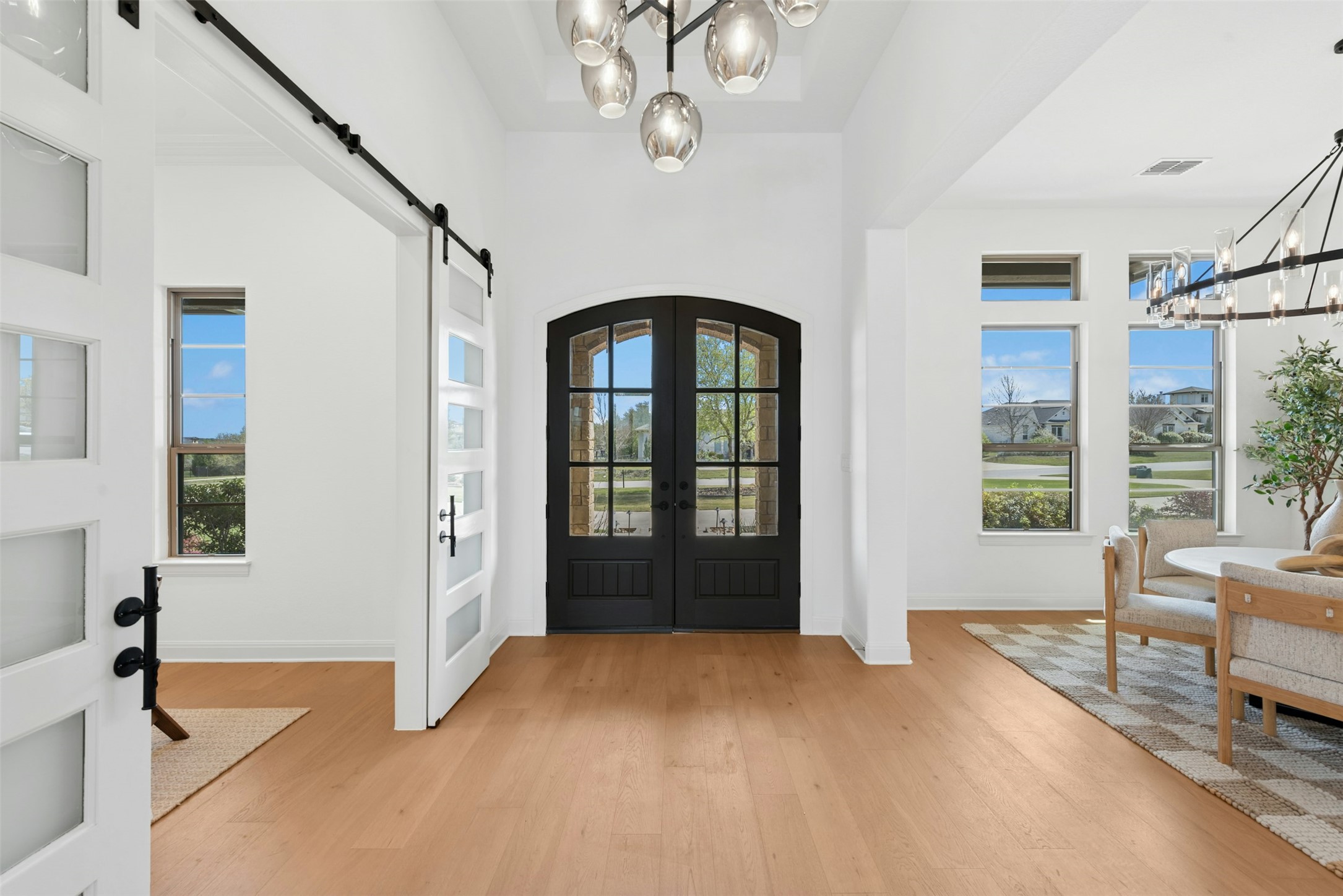 401 Brave Face Street Leander, TX 78641 - Photo 6 of 35 Foyer entrance with suspended lighting, french doors, light wood-style flooring, a barn door, and a high ceiling