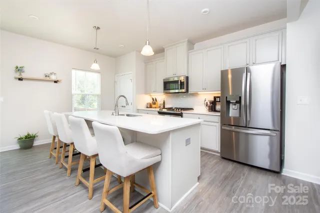 a kitchen with stainless steel appliances a refrigerator a stove a sink dishwasher a dining table and chairs with wooden floor