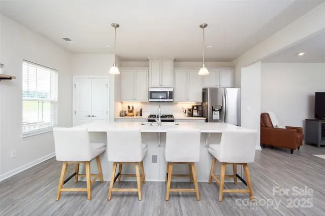 a kitchen with stainless steel appliances granite countertop a dining table chairs refrigerator and microwave