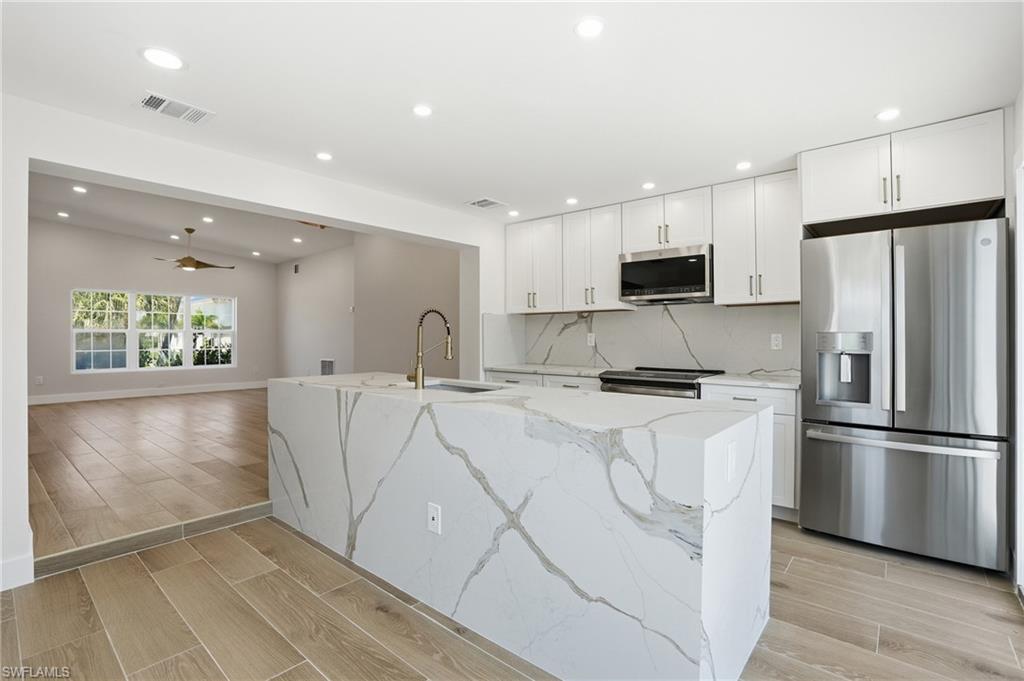 8336 Lagoon Road Fort Myers Beach, FL 33931 - Photo 11 of 50 The kitchen features a large island with a waterfall edge and integrated sink, stainless steel appliances, and white cabinetry - Virtually Edited Image