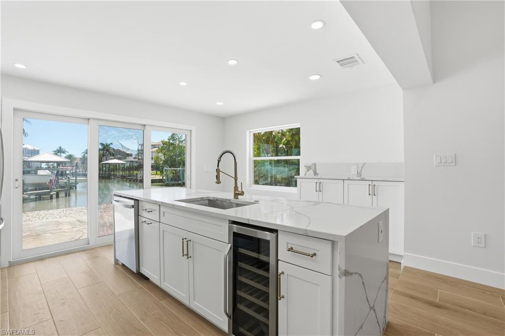 8336 Lagoon Road Fort Myers Beach, FL 33931 - Photo 12 of 50 Kitchen featuring an island with a built-in sink, dishwasher, and beverage cooler, white cabinetry, and light-colored countertops - Virtually Edited Image