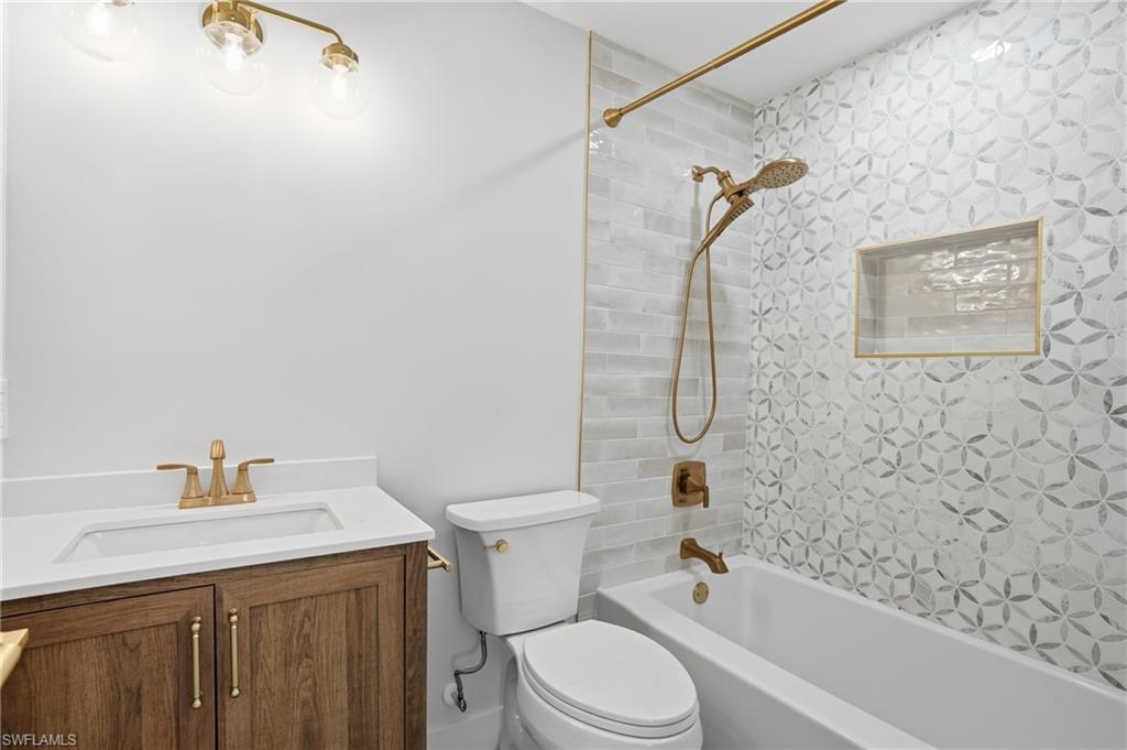 8336 Lagoon Road Fort Myers Beach, FL 33931 - Photo 18 of 50 Bathroom featuring a vanity with a white countertop and wood cabinetry, a white toilet, and a white bathtub with a tiled surround - Virtually Edited Image