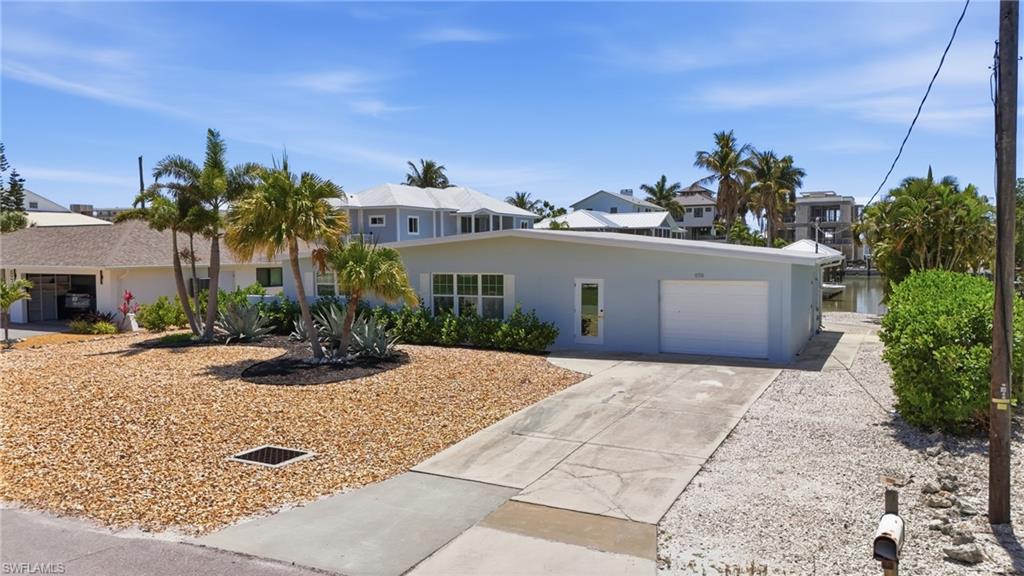 8336 Lagoon Road Fort Myers Beach, FL 33931 - Photo 44 of 50 The property features a concrete driveway leading to a garage, a gravel yard with mature palm trees, and views of a canal - Virtually Edited Image