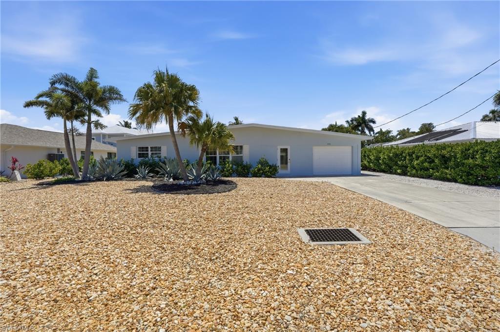 8336 Lagoon Road Fort Myers Beach, FL 33931 - Photo 49 of 50 The property features a light-colored exterior with a white garage door, a concrete driveway, and a gravel-covered yard - Virtually Edited Image