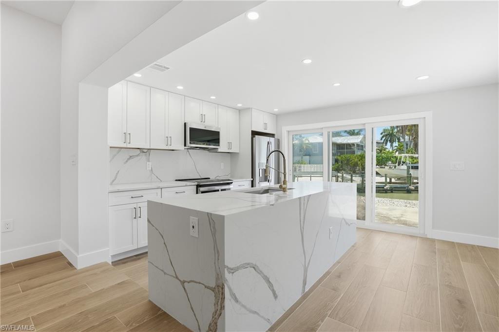 8336 Lagoon Road Fort Myers Beach, FL 33931 - Photo 10 of 50 Modern kitchen featuring light wood-style flooring, white cabinetry, a large kitchen island, and a stainless steel refrigerator - Virtually Edited Image