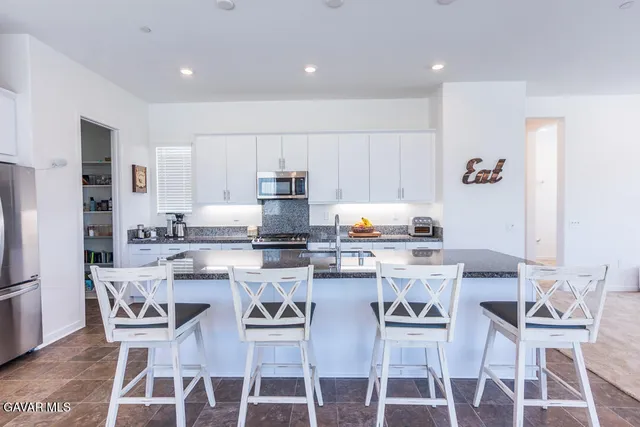 a kitchen with stainless steel appliances kitchen island granite countertop a dining table chairs refrigerator and microwave