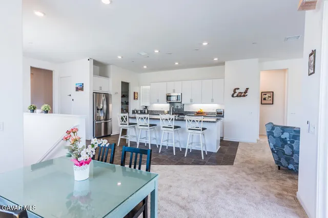 a kitchen with stainless steel appliances granite countertop a dining table chairs sink and white cabinets