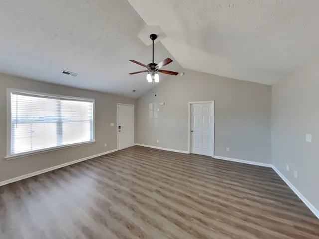 an empty room with wooden floor fan and windows