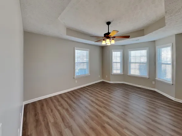 an empty room with wooden floor chandelier fan and windows
