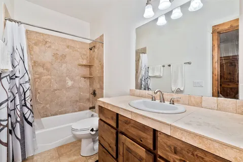 a bathroom with a granite countertop sink a toilet a mirror a bathtub and shower