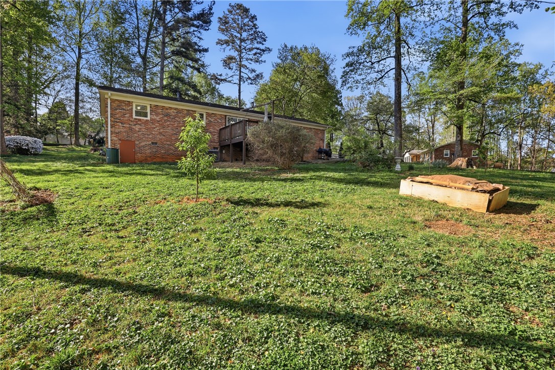 623 West Springwood Drive Seneca, SC 29672 - Photo 25 of 50 This spacious yard features lush green grass, towering trees, and a charming brick exterior with a wooden deck.