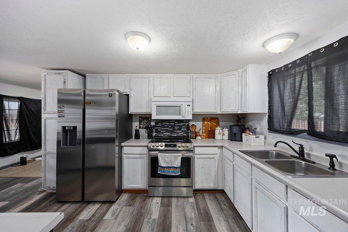 418 South Date Street Shoshone, ID 83352 - Photo 11 of 36 Kitchen featuring white cabinetry, stainless steel appliances, a double basin sink with a matte black faucet, wood-finish flooring, and a tiled backsplash