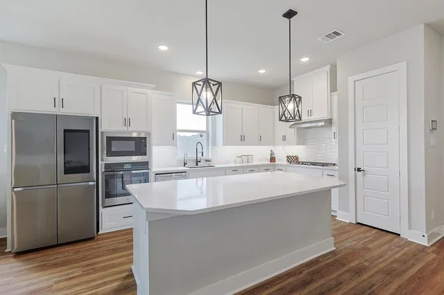 a large kitchen with kitchen island a stove a sink a center island and wooden floor